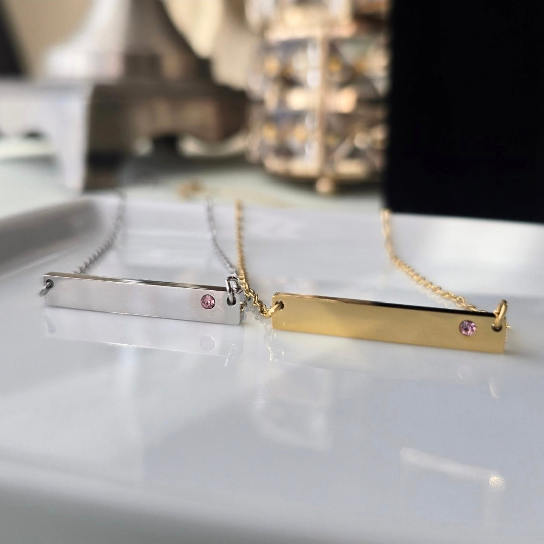 Two elegant birthstone necklaces with pink tourmaline gems on silver and gold bars displayed on a white surface