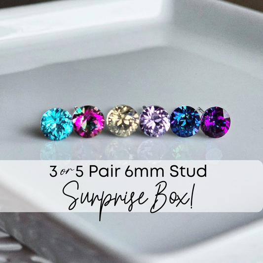 Six pairs of colorful gemstone stud earrings on a white tray with text overlay that says "3 or 5 pair 6 millimeter stud surprise box."