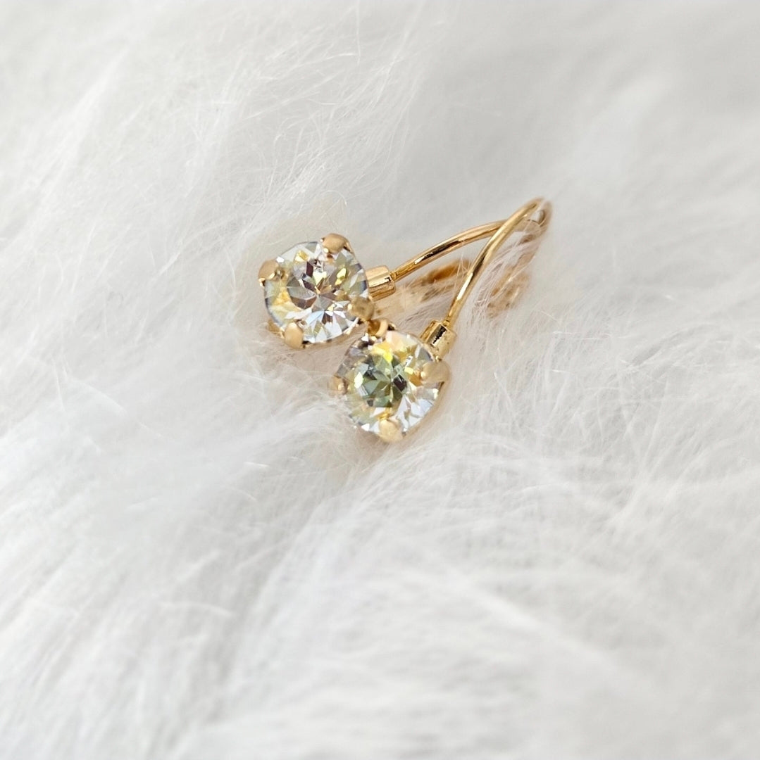 Image features a pair of gold plated french lever back earrings with a 6mm crystal gem. The earrings are nestled in a soft white fur pillow.