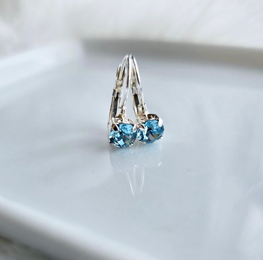 Small Aquarmarine stones in a silver french lever back setting on a white background.