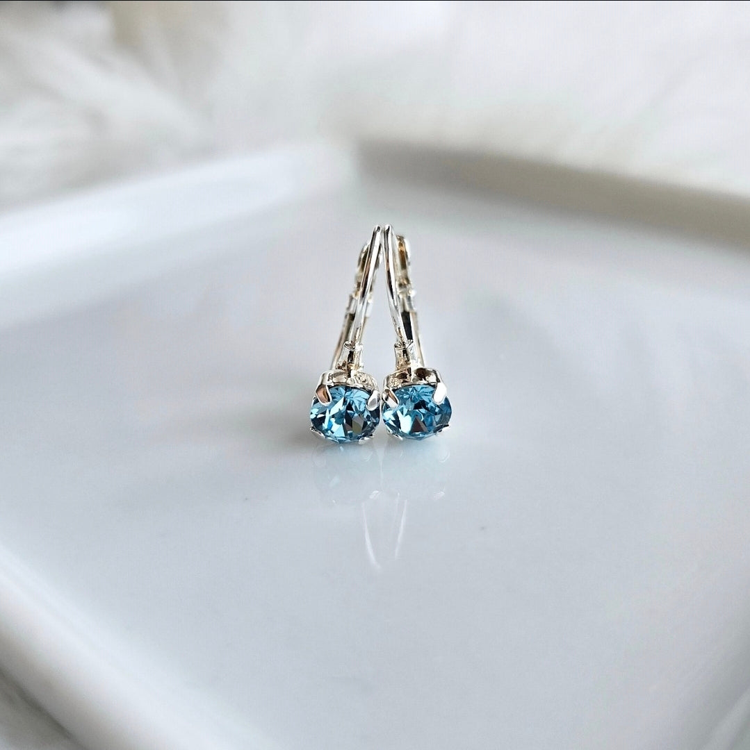 Small Aquarmine Blue stones in a silver french lever back setting on a white background.