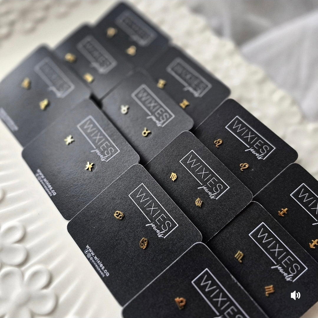 Small Zodiac Sign Studs in gold tone displayed on black Wixies branded cards, delicate and stylish PVD plated design