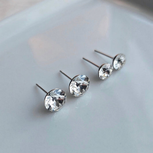 Two pairs of Wixies "Ice" 8mm or 6mm Studs with clear sparkling gems and stainless steel posts on a smooth surface
